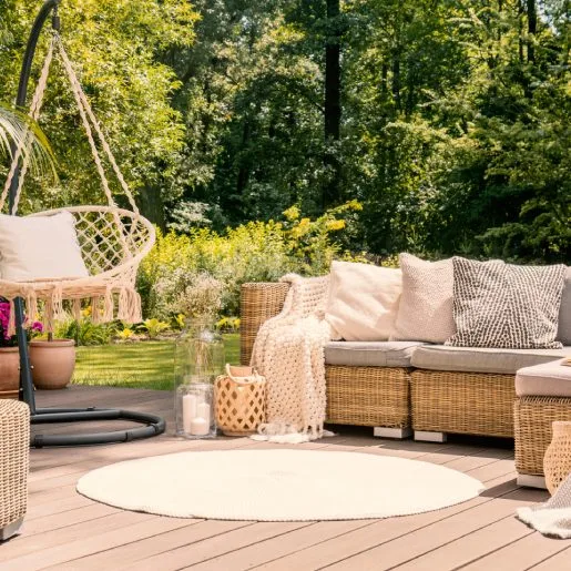 A big terrace with a comfortable leisure sofa with cushions, a table and a string swing in a green garden during sunny vacation.