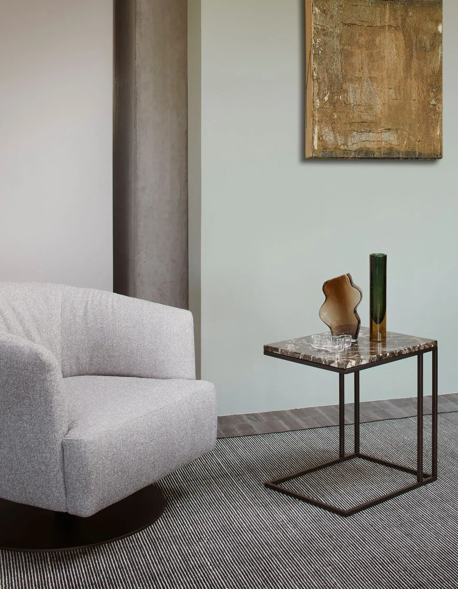 2b_NICOLINE_DIGA-SWIVEL_zKX31cYEFW gray fabric snug looking circular swivel arm chair on round black base in an empty room against a mint wall.